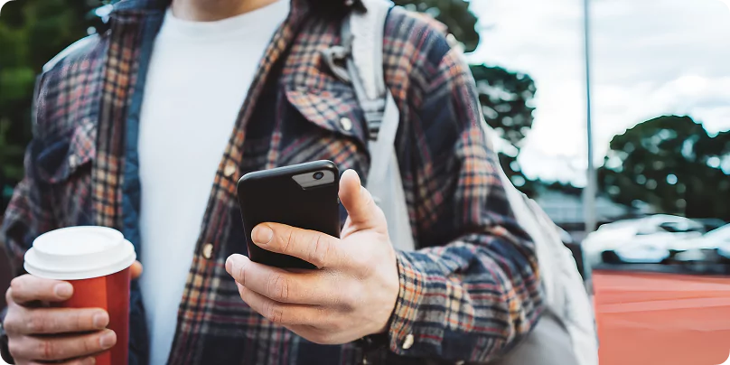 Person in plaid jacket using smartphone while holding coffee outside a mining village accommodation area.