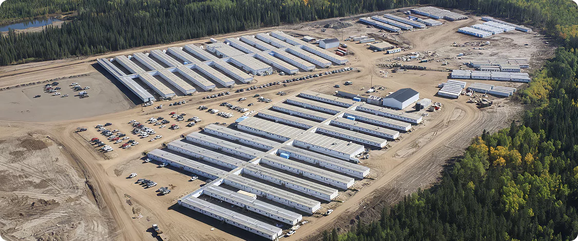 Large-scale workforce accommodation camp in a remote forested area, with modular buildings and support infrastructure.