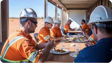 Crew members in high-visibility workwear eating lunch together in a remote site catering and dining facility.
