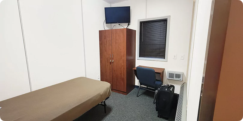 Interior of a remote site workforce accommodation room with single bed, desk, wardrobe, and mounted TV.