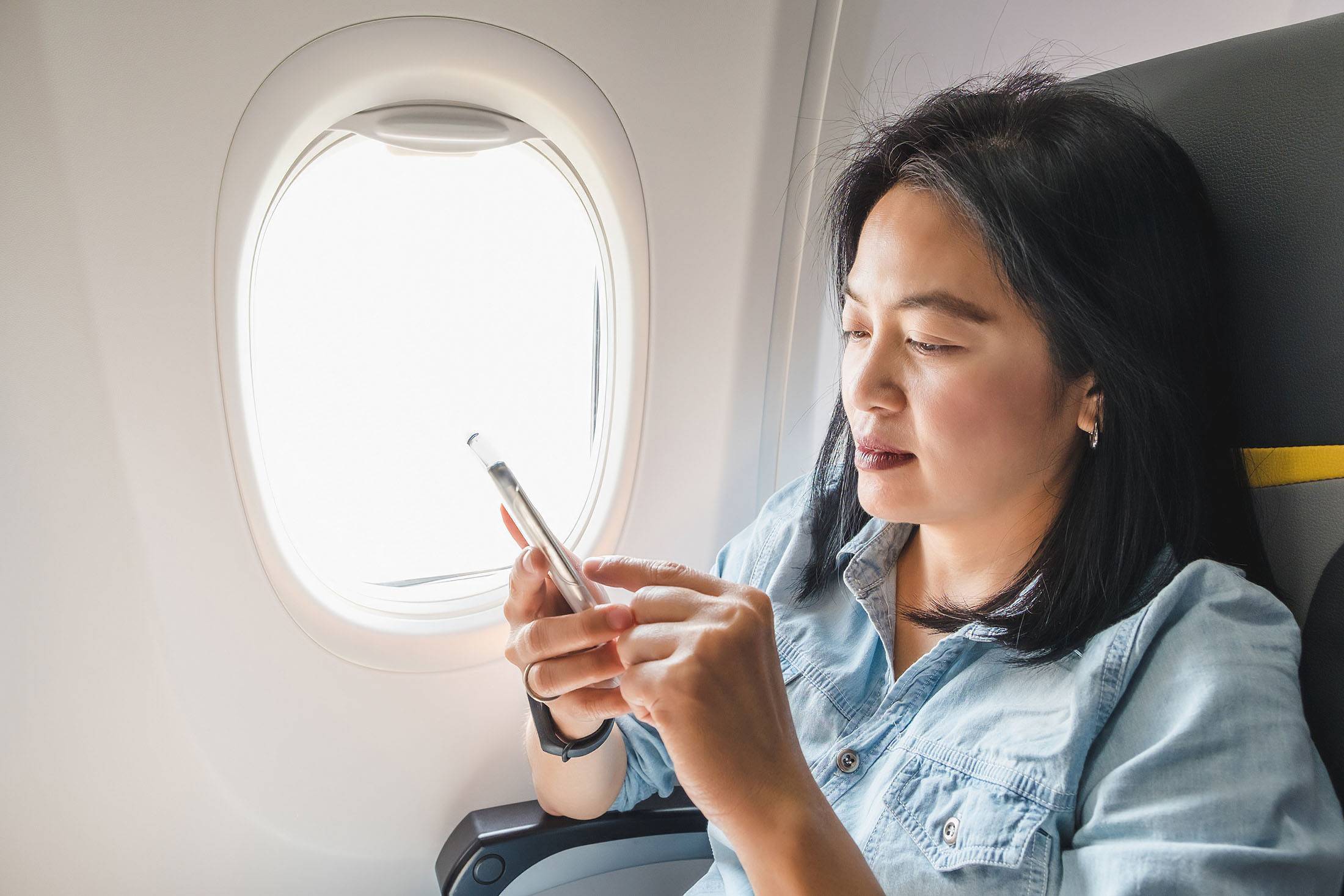 woman-typing-cell-phone-window-seat-plane