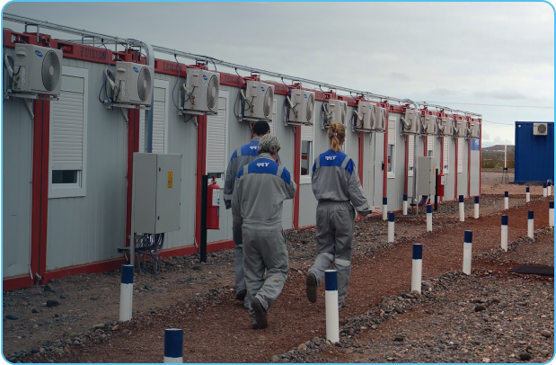 FIFO workers in personal protective equipment walk alongside camp buildings in desert setting.