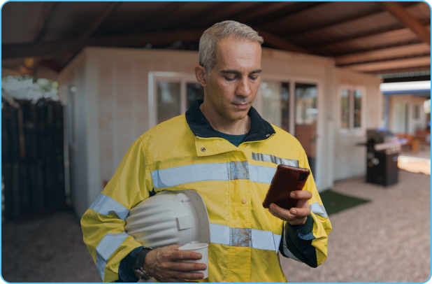 Fifo workers holds coffee and reads phone outside of camp bedroom constructed of prefabricated materials.