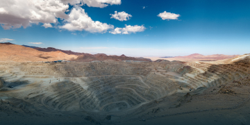 Aerial view of open pit mine with blue sky and clouds behind it.