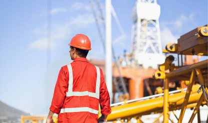 Oil and gas worker standing near a rig, wearing protective gear.