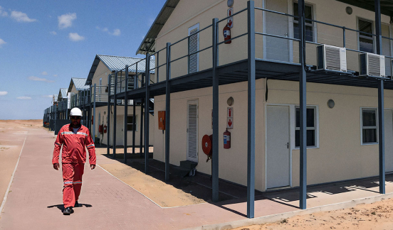 Worker walks along path next to semi-permanent oilfield accommodations set up in a remote desert location.