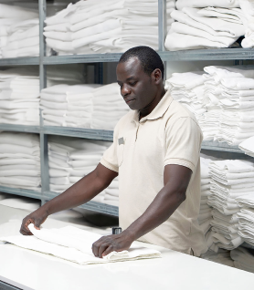 Housekeeping staff member folds towels in cleaning closet.