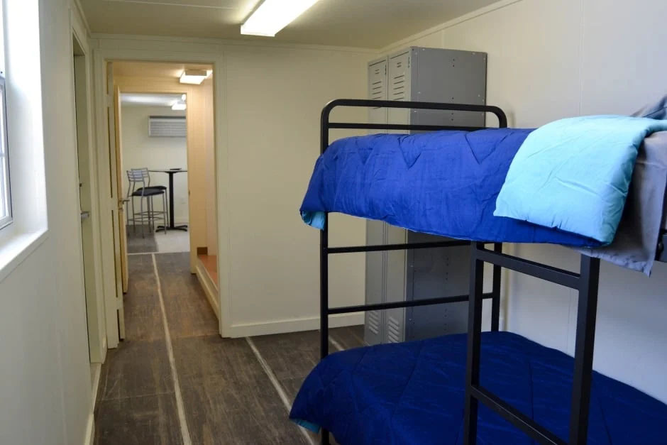 Two bunk beds in a room with a locker for clothing adjacent to them.