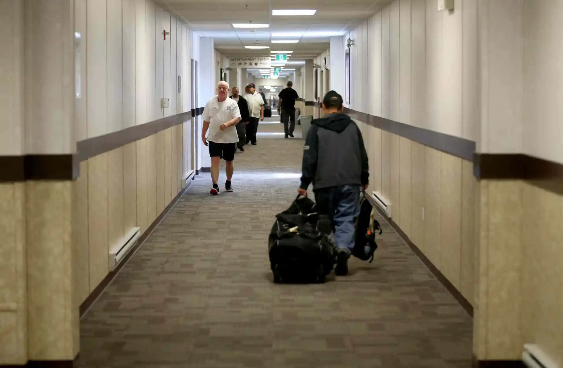 Workers walk down the long hallway of a work camp accommodation facility.