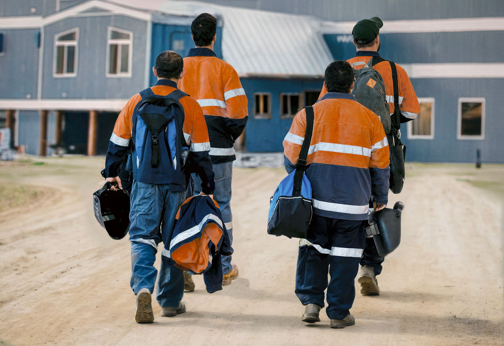 Fly-in fly-out workers walk on a dirt path towards the lobby of a mining camp.